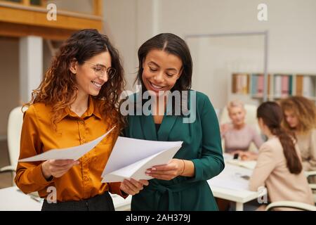 Due attraenti donne elegante scelta di miglior design sketch, i loro colleghi coworking dietro di loro Foto Stock