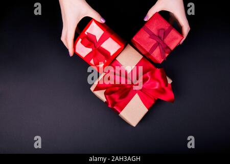 Donna di mani imbarcazioni carta scatole regalo con un regali per Natale e Capodanno, il giorno di san valentino o anniversario su sfondo nero, vista dall'alto Foto Stock