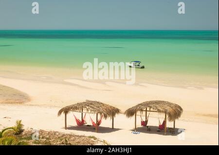 Palapa sulla spiaggia dei Caraibi con vista sul mare nell'isola di Holbox in Messico. I turisti si appoggiano su amache dall'oceano dei Caraibi Foto Stock