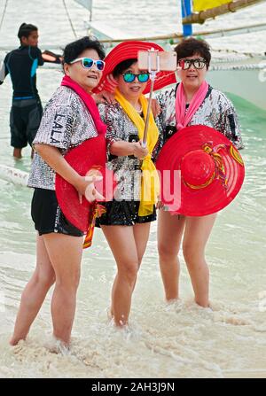 Il Boracay, Aklan Provincia, Filippine - 6 Gennaio 2018: tre donne cinesi turisti in costumi colorati che posano per una foto di gruppo con il loro cellulare ph Foto Stock