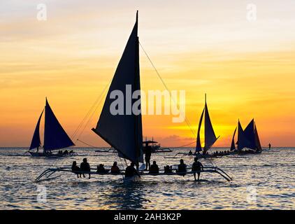 Il Boracay, Aklan Provincia, Filippine - 30 Gennaio 2018: sagome di filippini di barche a vela che trasportano i turisti sul loro quotidiano tramonto tours Foto Stock