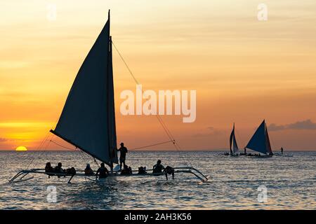 Il Boracay, Aklan Provincia, Filippine - 30 Gennaio 2018: sagome di filippini di barche a vela che trasportano i turisti sul loro quotidiano tramonto tours Foto Stock