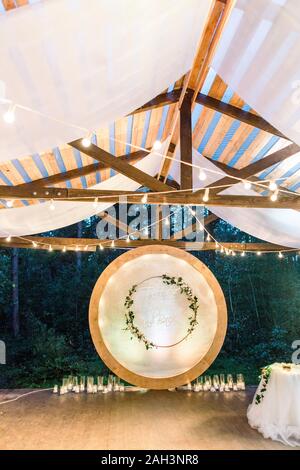 Nozze arco tondo in stile rustico decorato con ghirlande di fiori e vegetazione, retro lampadine sul soffitto. Bellissimo matrimonio istituito. Area o Foto Stock