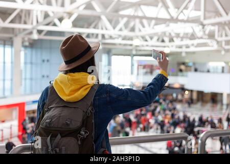 Vacanza Selfie. Bella giovane donna nel cappello e camicia di jeans tenendo selfie durante l'attesa per l'imbarco in aeroporto. Foto Stock