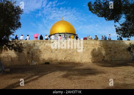 Un gruppo di visitatori in abiti colorati si riposa sulle pareti del Monte del Tempio con cupola della roccia sullo sfondo, visto nella vecchia Gerusalemme, Israele. Foto Stock