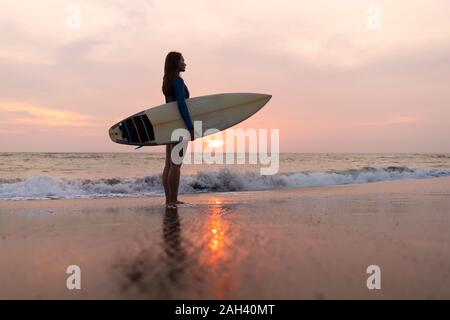 Giovane donna con la tavola da surf in spiaggia, Kedungu Beach, Bali, Indonesia Foto Stock