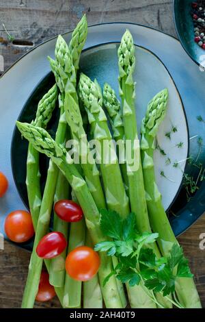 Piatti e ciotole con freschi pomodori ciliegia, asparagi, prezzemolo, il crescione e pepe Foto Stock