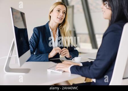 Due imprenditrici seduto alla scrivania in ufficio a parlare Foto Stock