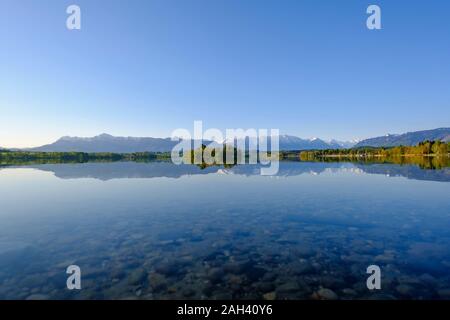 In Germania, in Baviera, Uffing am Staffelsee, vista panoramica del lago Staffelsee riflettendo cielo chiaro e sulle montagne circostanti Foto Stock