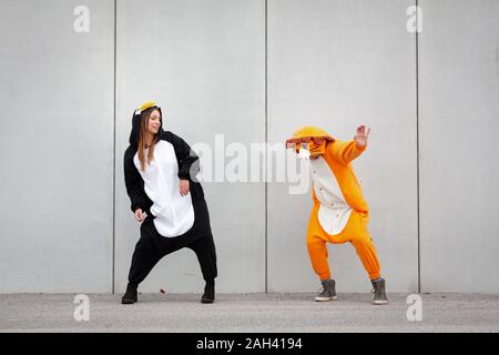 Due donne in penguin e lion costume nella parte anteriore della parete di cemento Foto Stock