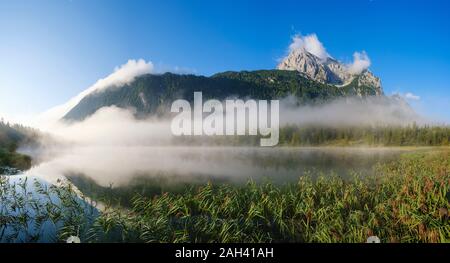 In Germania, in Baviera, Mittenwald, nebbia spessa che fluttua sopra il lago Ferchensee con Wettersteinspitzen mountain in background Foto Stock
