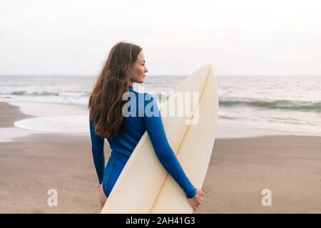 Giovane donna con la tavola da surf in spiaggia, Kedungu Beach, Bali, Indonesia Foto Stock