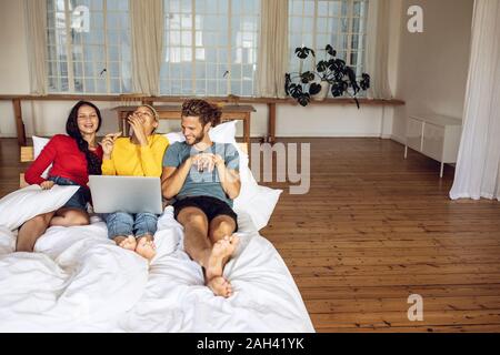 Happy amici rilassante nel letto a casa a guardare un film sul computer portatile Foto Stock