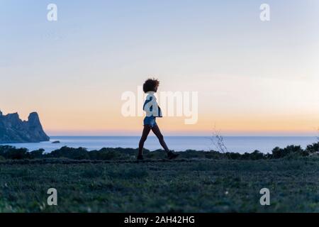 Giovane Donna che cammina su un prato al tramonto, Ibiza Foto Stock