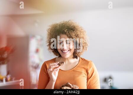 Sorridente metà donna adulta di mangiare un cookie Foto Stock