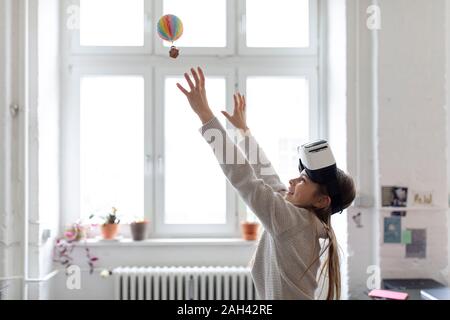 Ragazza con gli occhiali VR cercando di catturare in mongolfiera in office Foto Stock