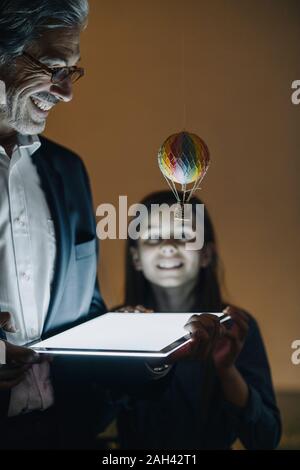 Felice buisinessman senior e la ragazza con mongolfiera e splendente tablet in ufficio Foto Stock