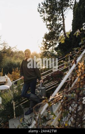 Felice donna in piedi sulle scale nel suo giardino, sorridente Foto Stock