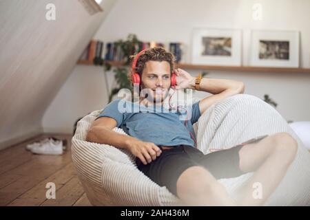 Giovane uomo rilassante in beanbag a casa ascolto di musica Foto Stock