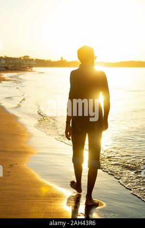 Uomo a camminare sulla spiaggia al tramonto, Warnemuende, Germania Foto Stock