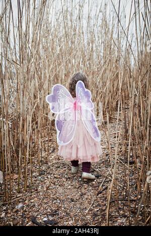 Vista posteriore della bambina in natura vestita come una farfalla Foto Stock