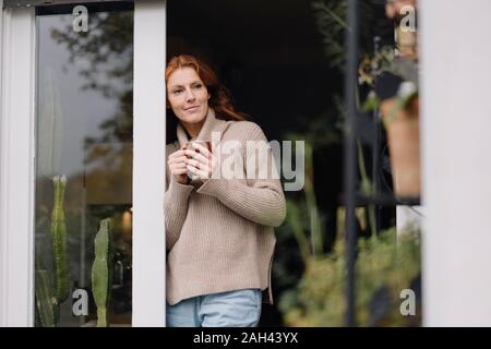 Donna appoggiata in porta, bere caffè Foto Stock