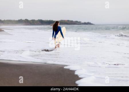 Giovane donna con la tavola da surf in spiaggia, Kedungu Beach, Bali, Indonesia Foto Stock