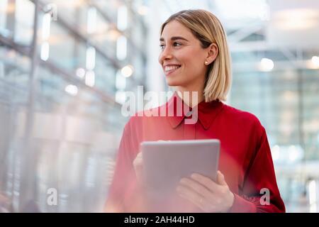 Sorridente giovane imprenditrice indossando maglietta rossa utilizzando tablet Foto Stock