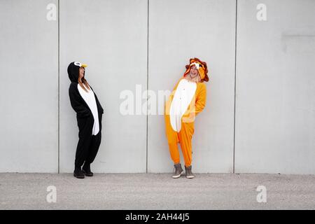 Due donne in penguin e lion costume nella parte anteriore della parete di cemento Foto Stock