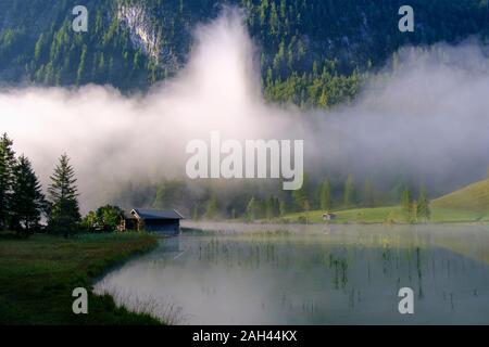 In Germania, in Baviera, Mittenwald, rifugio appartato in piedi sulla riva del lago Ferchensee con nebbia spessa in background Foto Stock