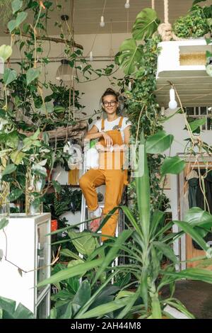 Ritratto di una giovane donna in piedi su una scala in un piccolo negozio di giardinaggio Foto Stock