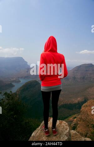 Donna in piedi su una roccia godendovi lo splendido paesaggio al di sotto di lei, Blyde River Canyon, Sud Africa. Foto Stock