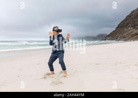 Imprenditore utilizzando occhiali VR sulla spiaggia, Nordhoek, Western Cape, Sud Africa Foto Stock