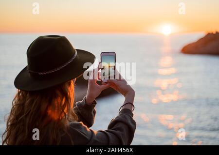 Giovane donna utilizza lo smartphone sulla spiaggia durante il tramonto, Ibiza Foto Stock