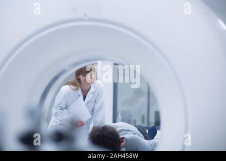 Paziente in ospedale durante esame CT, femmina radiologo sorridente Foto Stock