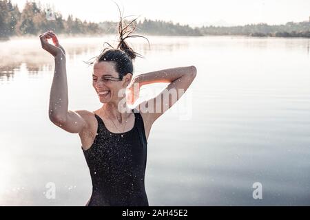Allegra donna vestita di nero costume da bagno in un lago a nebbia di mattina Foto Stock