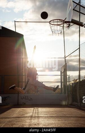 Adolescente giocare a basket, dunking contro il sole Foto Stock