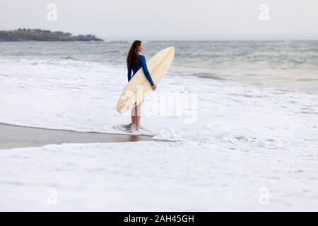 Giovane donna con la tavola da surf in spiaggia, Kedungu Beach, Bali, Indonesia Foto Stock