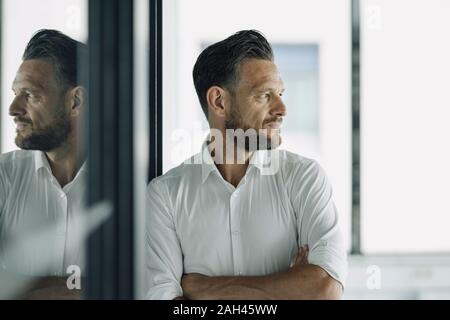 Imprenditore maturo appoggiata contro la parete di vetro in Office cerca lateralmente Foto Stock