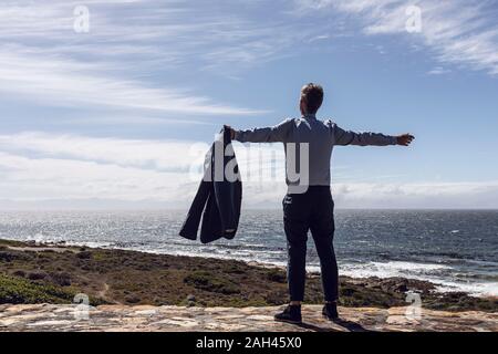 Vista posteriore di imprenditore in piedi di fronte al mare, a Cape Point Western Cape, Sud Africa Foto Stock