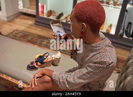 Giovane donna con taglio di capelli colorati di scattare una foto con il suo telefono di un paio di scarpe per acquistare in un negozio di abbigliamento Foto Stock