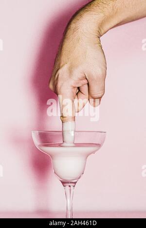 L'uomo immergendo il suo dito in un liquido in un bicchiere Foto Stock