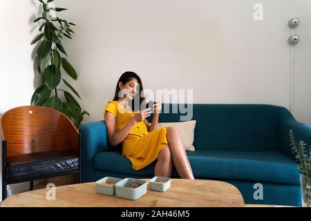 Sorridente giovane donna seduta sul lettino mediante telefono cellulare Foto Stock