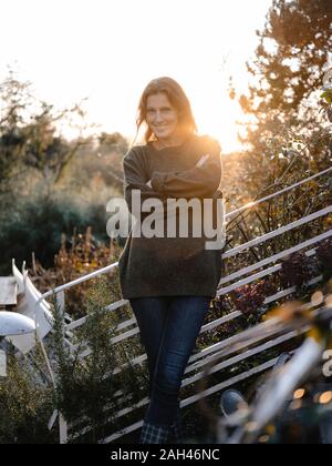 Felice donna in piedi sulle scale nel suo giardino, sorridente Foto Stock