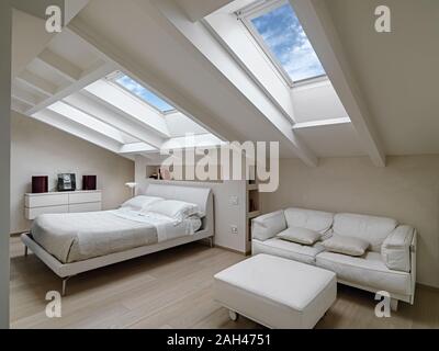Interior shot di una camera da letto in mansarda moderno-camera in primo piano i divani in pelle con poggiapiedi in background vi è il letto b illuminato Foto Stock