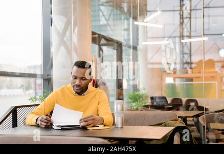 Uomo con tazza riutilizzabile la lettura dei documenti in un cafe Foto Stock