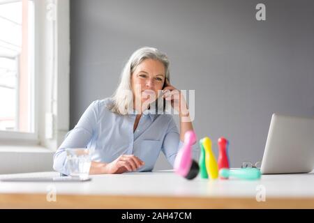 Imprenditrice matura al telefono giocando con i perni sulla scrivania in ufficio Foto Stock
