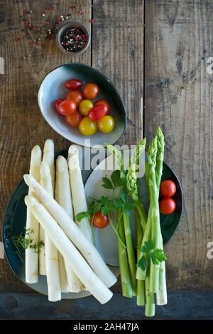 Piatti e ciotole con freschi pomodori ciliegia, verde e asparagi bianchi, prezzemolo, il crescione e pepe Foto Stock