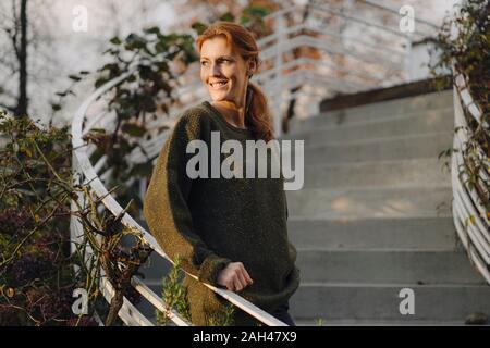 Felice donna in piedi sulle scale nel suo giardino, sorridente Foto Stock