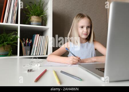 Ragazza seduta a tavola a casa a fare i compiti e utilizzo di computer portatile Foto Stock